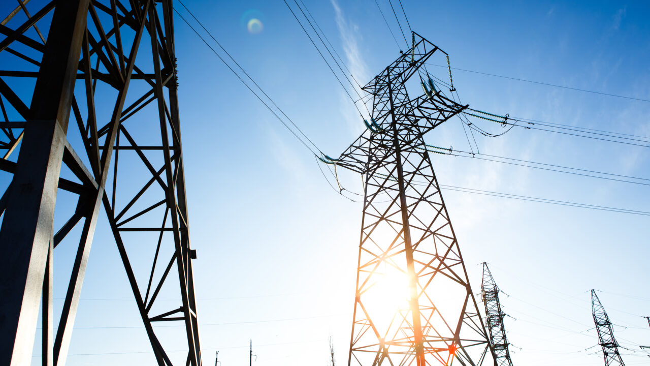 Pylônes électriques et lignes à haute tension sous un ciel bleu, illustrant les enjeux énergétiques et la performance des logements neufs conformes à la RE2020